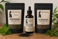 Queen Tee’s Wellness Bundle featuring black resealable bags of peppermint and echinacea loose leaf teas with a brown glass black cumin seed tincture bottle on a wooden surface